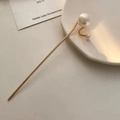 Detalle de una elegante horquilla dorada con perlas blancas sobre un plato de cerámica - F0230 Una Perla