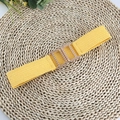 Detail of yellow elastic woven belt with a square interlocking gold metal buckle on straw mat - Yellow