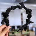 Detail of a black pleated satin headband with a knotted texture held by hand - Black (Cloth Pleated)