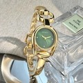 Detail einer Uhr mit grünem Zifferblatt, Hufeisengehäuse und goldener Armspange auf Leinenstoff - Grün