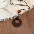 Close-up of vintage resin necklace with large brown pendant and amber bead on wood - Necklace-Black-Round