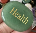 Close-up of green natural stone with gold Health engraving being held in a hand - Green Aventurine