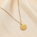 Detail of Libra constellation pendant on beaded gold chain over beige silk fabric - Libra
