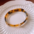 Detailed view of leopard print resin bangle with gold metallic accents on ceramic plate - Coffee (Tortoiseshell)