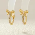 Close-up of gold bow earrings featuring sparkling zircon inlay on a display stand - ER0865-A (Gold Bow)