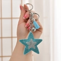 Sparkling blue sequin star keychain with tassel and bell held by hand in soft light - Sky Blue
