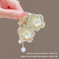 Gros plan détaillé de la pince à cheveux fleur dorée avec strass et pompons de perles - M58 Double Fleur à Cinq Pétales