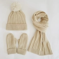 Detailed flat lay of beige cable knit winter set including pompom hat, scarf, and gloves - Off White