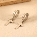Gros plan sur les boucles d'oreilles croix en acier argenté sur cuir blanc - Boucles d'Oreilles Créoles en Argent