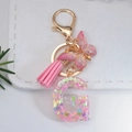Macro shot of resin letter G keychain with pink butterfly sequins and gold tassel details - Letter G