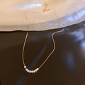 Macro shot of a gold geometric necklace with small white pearls on a reflective surface - Fine Chain Pearl Necklace / Gold