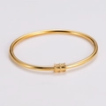Dettaglio di un bracciale rigido in acciaio dorato con tre cilindri a trama diamantata - Oro