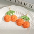 Detalle macro de pendientes de fruta tejidos a mano sobre un plato de cerámica decorativo - Naranja
