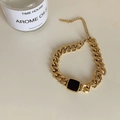 Goldenes Gliederkette-Armband mit einem schwarzen quadratischen Stein auf weißem Grund - Armband / Gold