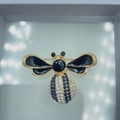 Golden bee brooch with blue crystals and black enamel wings on a white box - Style 27