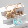 Detail van een zeekeychain met zeester, schelp en blauwe bal vol glitters - Blauw