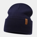 Close-up of a navy blue knitted beanie with a brown leather label and logo detail - Navy Blue
