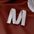 Dettaglio della luccicante spilla argento lettera M con strass su raso rosso scuro - 24# Letra M Cristalli Argento