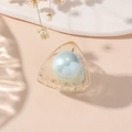 Detail of yellow transparent hair claw clip with large light blue pearl on beige surface - Triangle-Light Blue Pearl