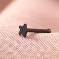 Macro shot of a black star-shaped stainless steel nose stud on a soft pink background - Black