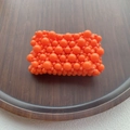 Detail of vibrant orange beaded texture with multi-size resin spheres on dark wood - Orange