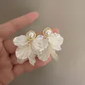Elegant white shell flower petal earrings with a central pearl in hand-held display - Pearl Petal Tassel Studs