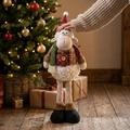 Detail of Christmas sheep plush with red plaid jacket and long legs by festive tree - Extendable Sheep (ML-Q780)