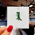Detail of cute green dinosaur enamel pin on display card held against a blurred background - 23*Green Dinosaur Pin