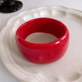 Close-up of a wide polished red resin bangle placed on a wavy textured ceramic plate - Bright Red