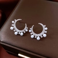 Macro shot of silver C-shaped earrings with sparkling cubic zirconia and white pearls - Silver