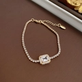 Close-up of golden square zircon bracelet with S925 hallmark tag on textured background - Bracelet (Gold)