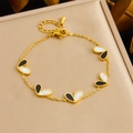 Goldenes Armband mit schwarz-weißen Herzanhängern auf einem weichen Goldkissen - Einzelstück (Armband)