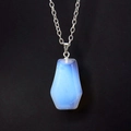 Macro shot of light blue hexagon opal pendant on silver chain against black background - Opal