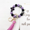 Detail of beaded keychain with cross charm and pink leather tassel on wood background - Purple Black