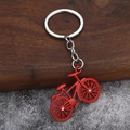 Red metal bicycle keychain with sparkling rhinestone wheels on rustic wood background - Red