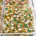 Close-up of bulk gold cherry pendants with green and white zircons in a storage box - White
