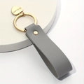 Grey leather keychain with gold heart charm engraved with He is love on white base - Gray