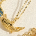 Macro-opname van een gouden walvis hanger met blauwgroen emaille en een fijne gouden ketting - Haai Ketting