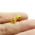 Detalle macro de dos cuentas espaciadoras de aleación dorada con forma de flor en un dedo - Oro Brillante