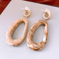 Primer plano de pendientes ovalados de acrílico ámbar con un diseño retro exagerado - Poste de plata para pendientes - Café