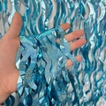 Hand holding vibrant blue S-shaped wavy foil fringe curtain with shimmering glitter finish - Laser S-Shape / Light Blue