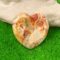 Heart-shaped thumb worry stone with natural red and brown patterns on green grass - Crazy Agate