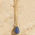 Close-up of blue enamel egg pendant with gold spiral lines on a gold chain necklace - Sapphire Blue