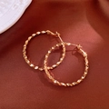 Detalle de pendientes de aro dorados con facetas de diamante en seda roja - Estilo de Aro con Facetas Geométricas / Dorado