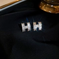 Detailopname van goud vergulde H-vormige oorbellen met glinsterende diamanten op stof - Gouden Letter H Pavé Diamanten Oorknopjes (8#)