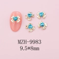 Macro view of 9.5x8mm gold bow nail charms with blue heart crystal on pink manicure - Gold Bow + Blue Heart Stone (9983)