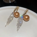 Dettaglio di orecchini con perle dorate e nappe scintillanti su un piatto bianco puro - Oro con perla arancione (HE22622)