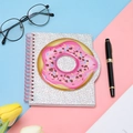 Detail of glitter notebook with pink 3D donut patch and spiral binding on blue background - Donut