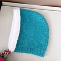 Detailed texture of blue knitted baby bonnet featuring colorful tassel poms and ties - Lake Blue