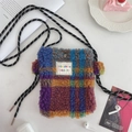 Close-up of a rainbow checkered plush mini shoulder bag with drawstring strap on a desk - Multi Color Grid